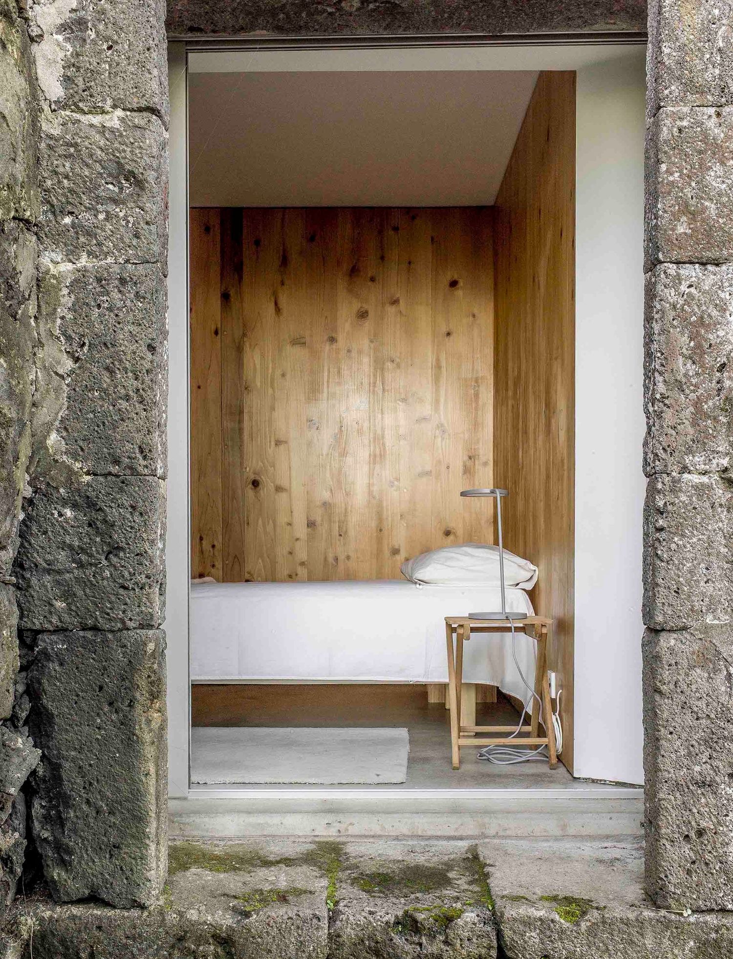 E/C House by SAMI-arquitectos — Interior view through a stone threshold reveals a timber-lined bedroom chamber.