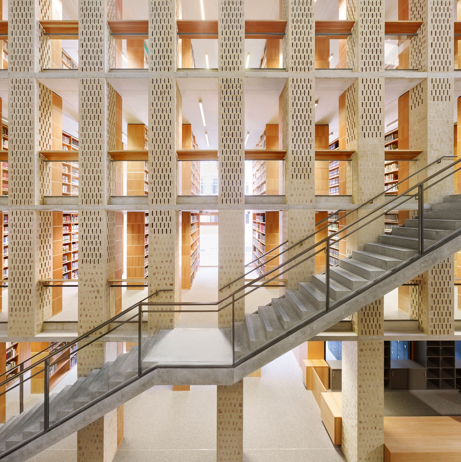 Philosophical Seminar at the Cathedral Square by Peter Böhm Architekten — A multi-story atrium viewed from a diagonal staircase that bridges concrete floors and perforated brick columns.