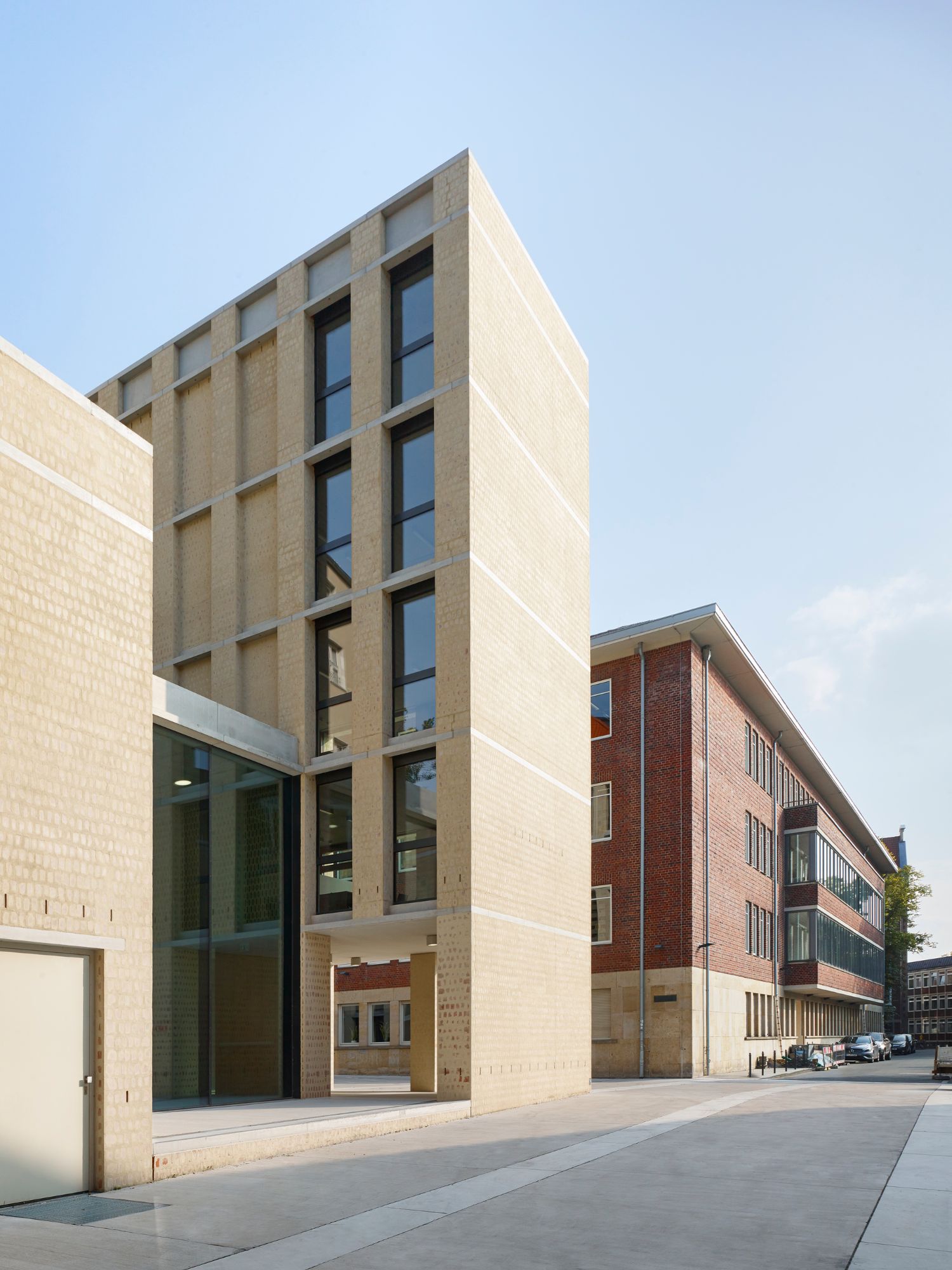Philosophical Seminar at the Cathedral Square by Peter Böhm Architekten — The Philosophikum's sand-colored brick facade demonstrates a perforated pattern of vertical window slots ascending the narrow street-facing elevation.