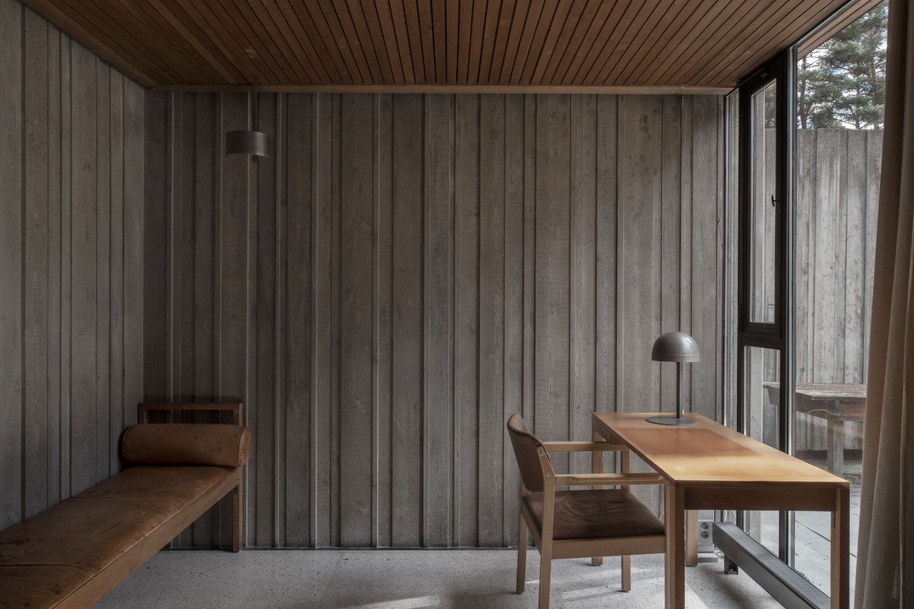 Gävle Crematorium by ELLT captured by Andy Liffner — A timber-lined interior study or meditation room features vertically board-formed wood walls in weathered grey tones, with a matching slatted ceiling overhead.
