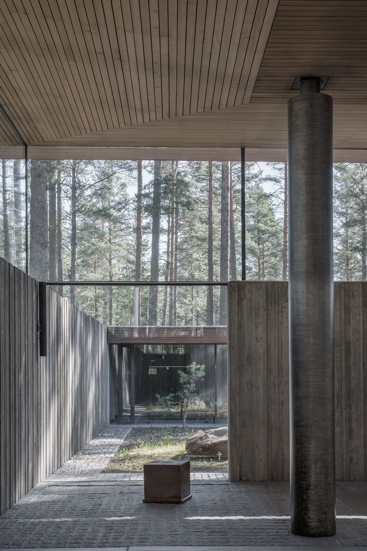 Gävle Crematorium by ELLT captured by Andy Liffner — A covered passage frames the forest beyond through continuous glazing, its timber soffit contrasting with weathered concrete walls bearing visible patina.