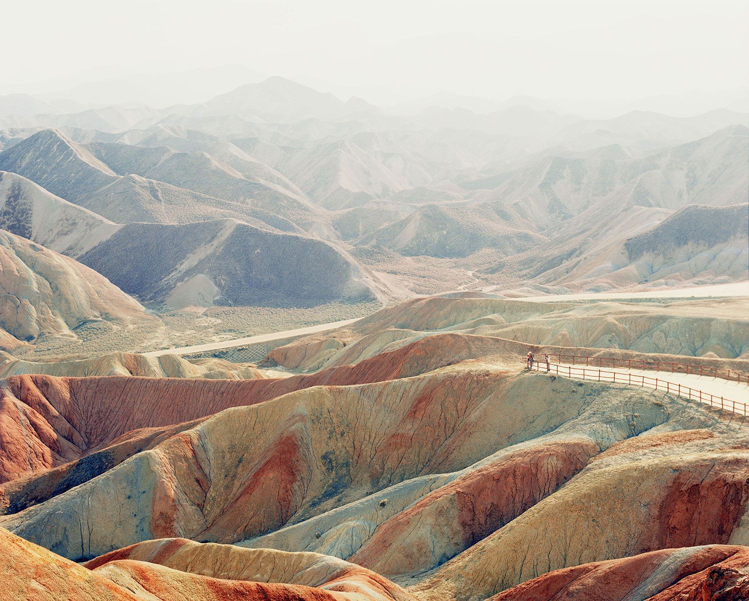 Universal Experience by Catherine Hyland — Hyland's photograph captures a serpentine river cutting through heavily eroded mountains with distinctive polychromatic striations—rust-red, ochre, sage,...