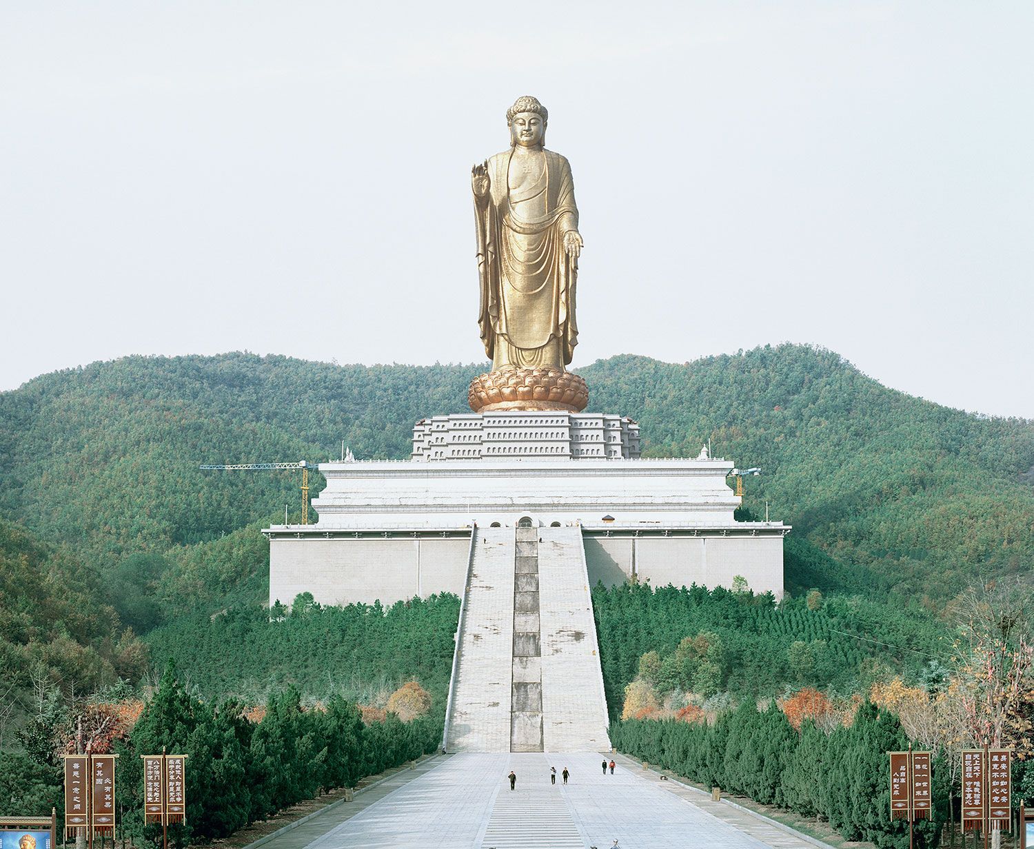 Universal Experience by Catherine Hyland — A monumental bronze Buddha statue rises 57 meters above a tiered concrete base with horizontal striations and guard railings.