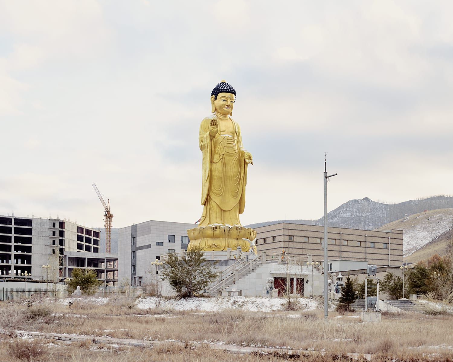 Universal Experience by Catherine Hyland — A colossal gilt bronze Buddha statue dominates the composition, positioned centrally at 57 meters tall with a raised right hand in blessing gesture.