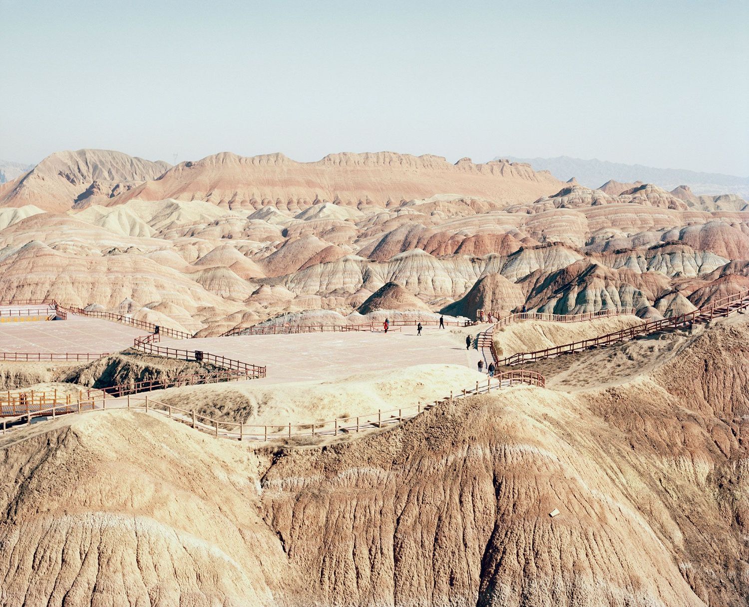 Universal Experience by Catherine Hyland — Earthen badlands formations dominate the composition, their stratified geological layers rendered in cream, taupe, and rust tones.