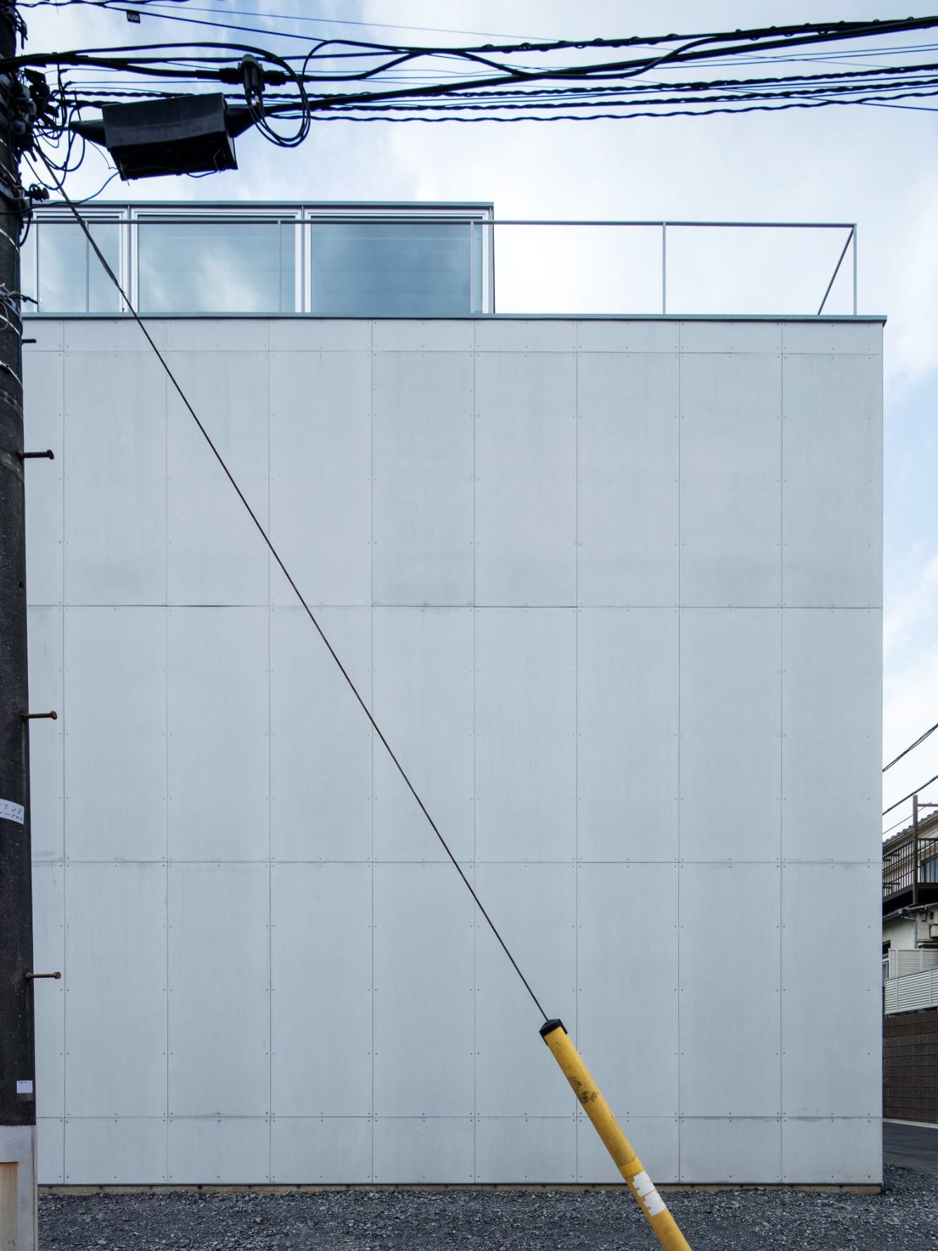Ebisu No Ie by Tetsuo Yamaji Architects — The south-facing facade of Ebisu No Ie presents a gridded white panel system punctuated by a diagonal yellow utility conduit.