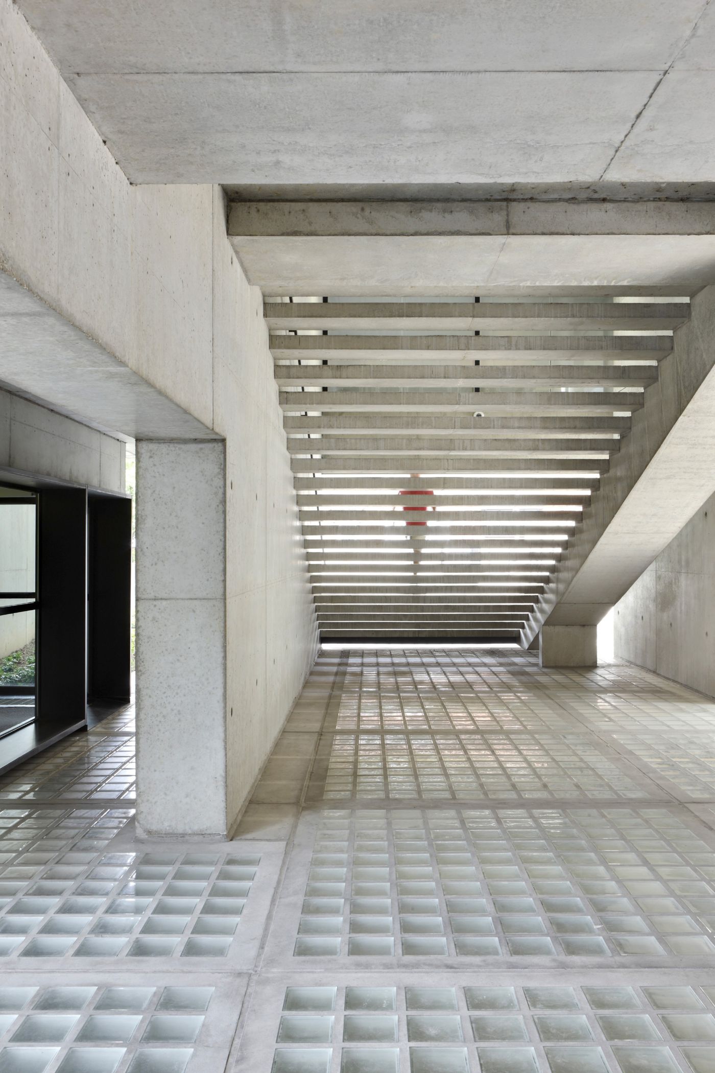 AZL Pension Fund Headquarters by Wiel Arets Architects by WAA Wiel Arets Architects — A concrete corridor extends into deep perspective, its ceiling defined by parallel white-painted timber beams that create rhythmic horizontal lines receding...