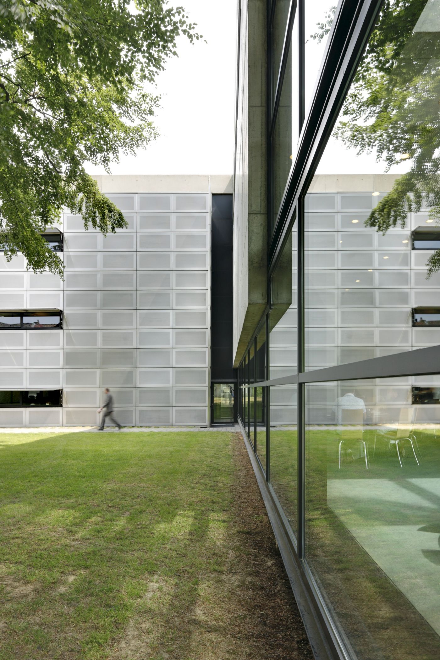 AZL Pension Fund Headquarters by Wiel Arets Architects by WAA Wiel Arets Architects — The courtyard view captures the architectural intervention between two concrete-faced wings, connected by a vertical black steel-framed glazed passage.