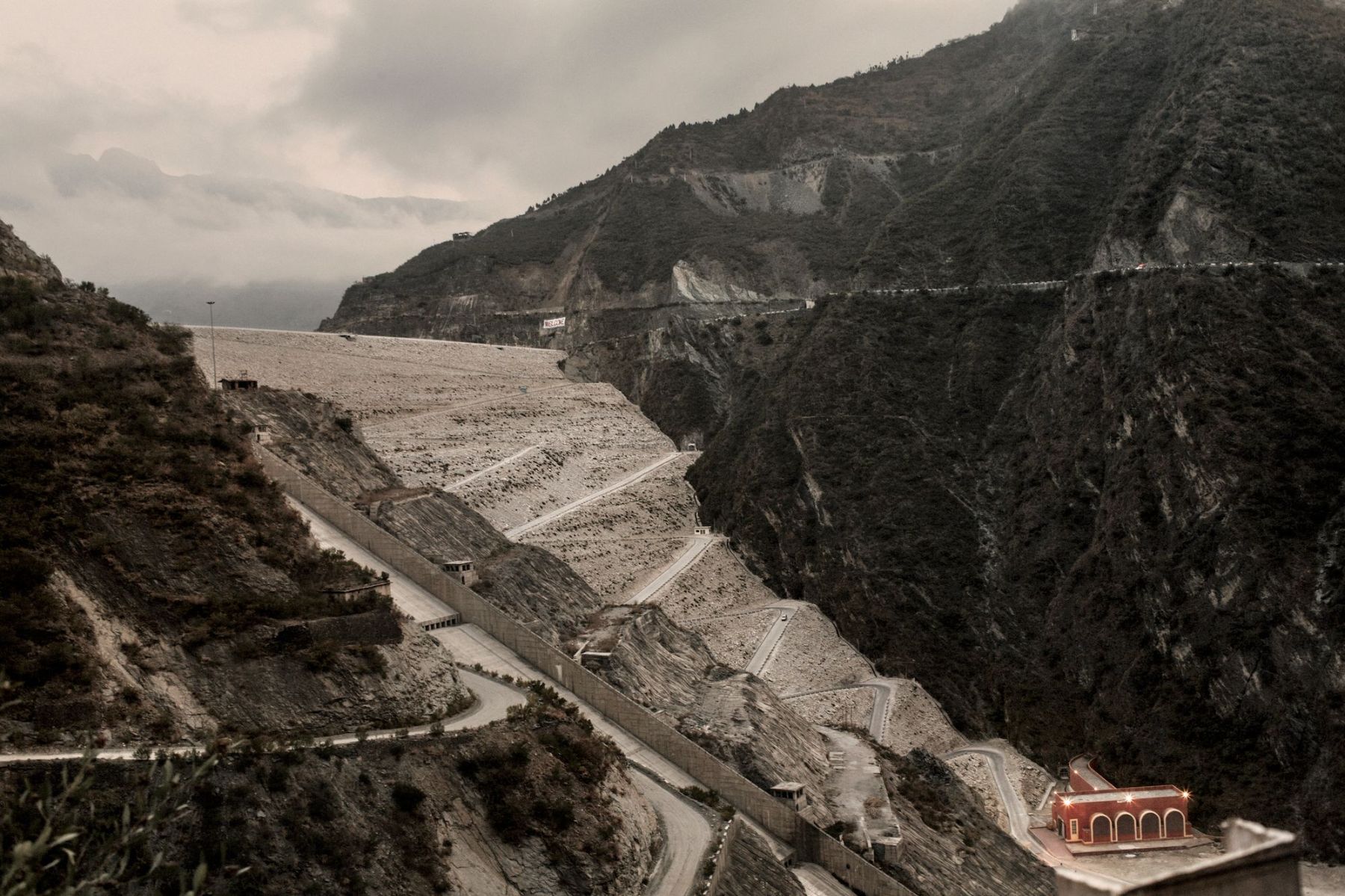 Ganga Ma by Giulio Di Sturco — A monumental concrete dam structure dominates the valley, its stepped spillway face angled toward the camera with geometric precision.