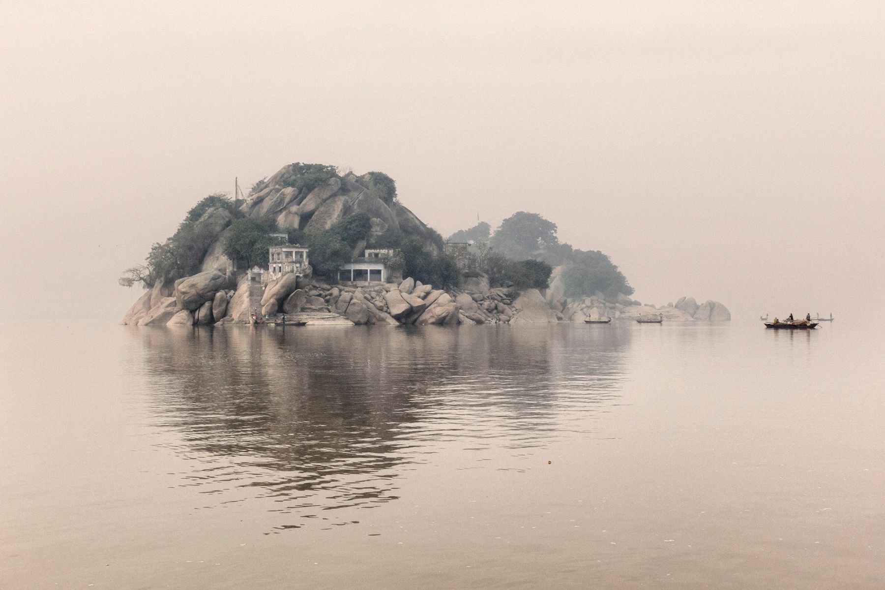 Ganga Ma by Giulio Di Sturco — A granite outcropping crowned with colonial-era structures emerges from still water in dense mist.