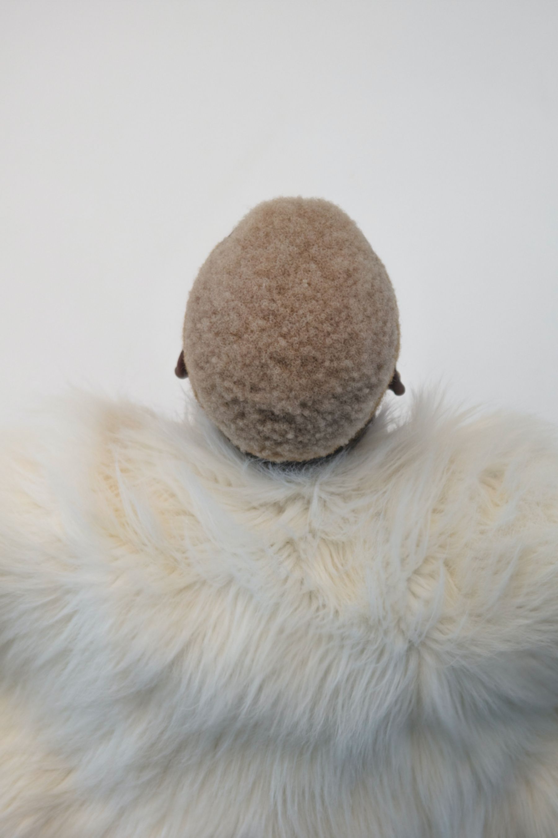 Selected works by Lakin Ogunbanwo — A sculptural form wrapped in cream-colored wool fabric dominates the composition, its egg-like silhouette rising from a nest of white fur.