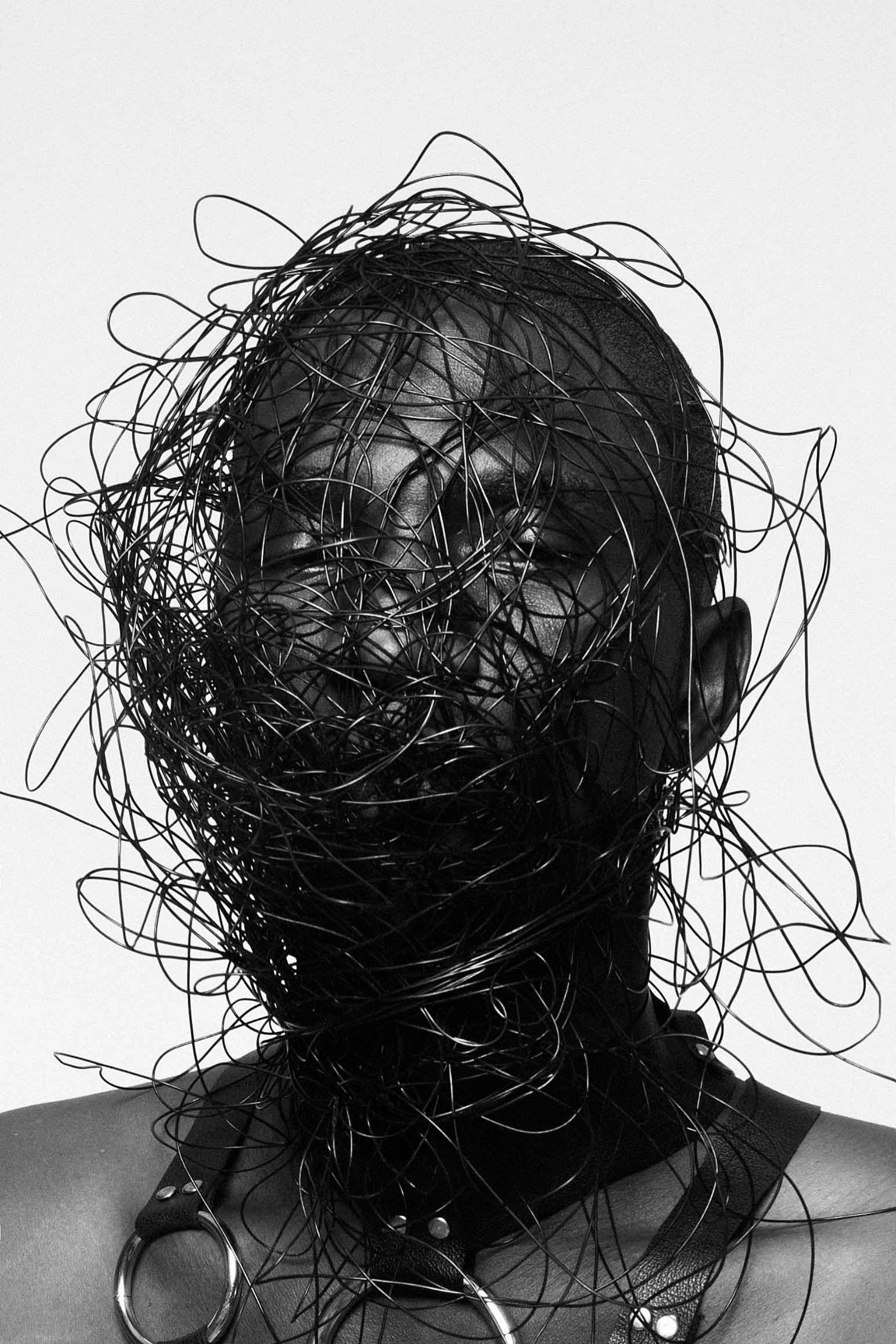 Selected works by Lakin Ogunbanwo — A black and white portrait photograph presenting a figure whose face and upper body are obscured by densely layered, tangled linear elements—resembling...