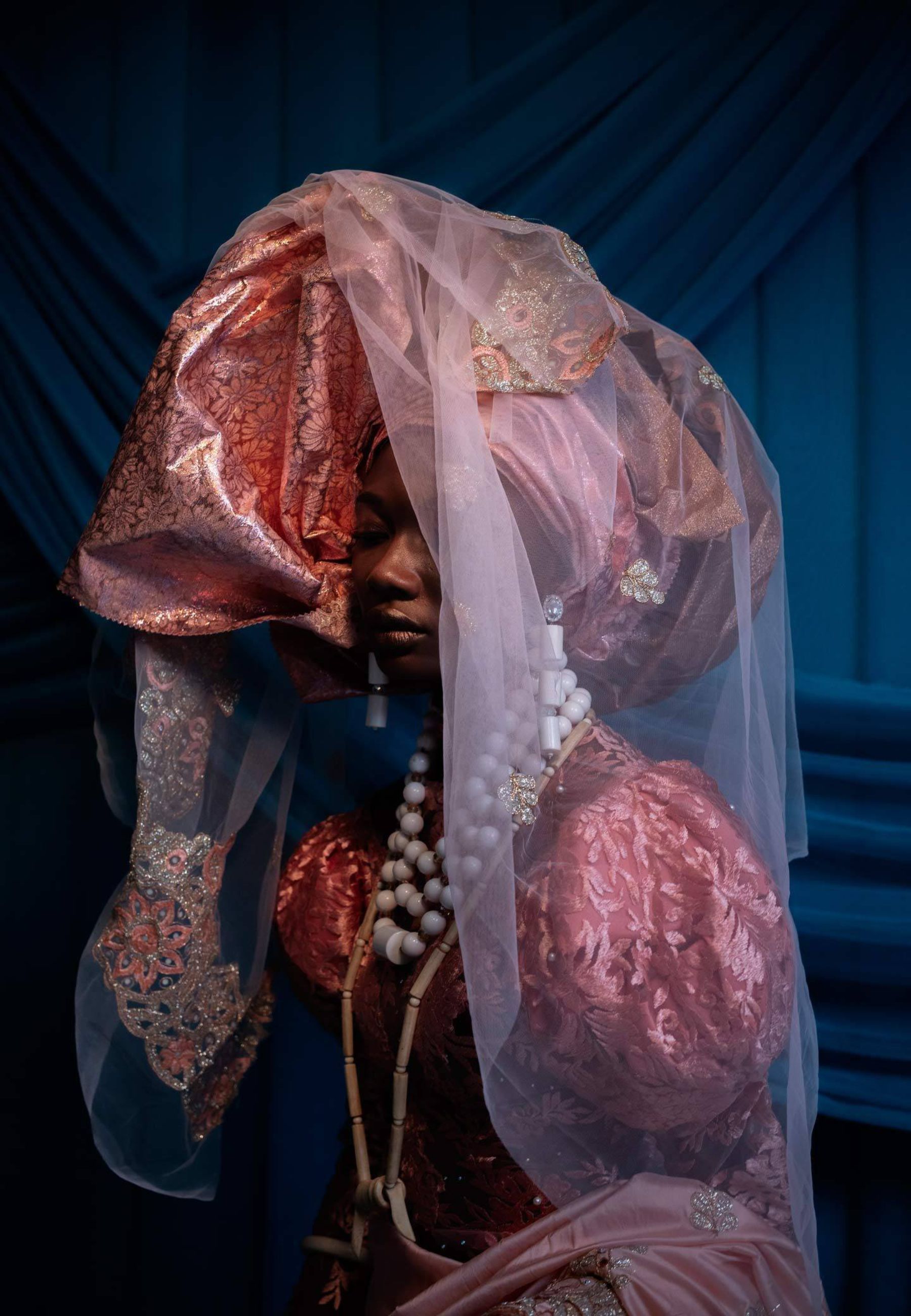 Selected works by Lakin Ogunbanwo — Portrait of a figure draped in layered textiles—deep burgundy patterned fabric with gold embroidery and a sheer mauve overlay—against a deep teal background.