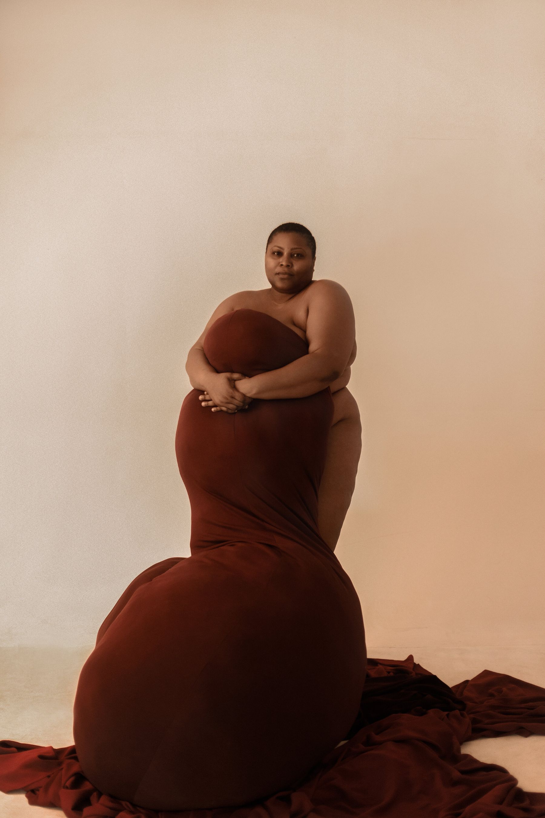 Selected works by Lakin Ogunbanwo — A portrait photograph featuring a single figure in a deep burgundy draped fabric positioned against a neutral beige background.