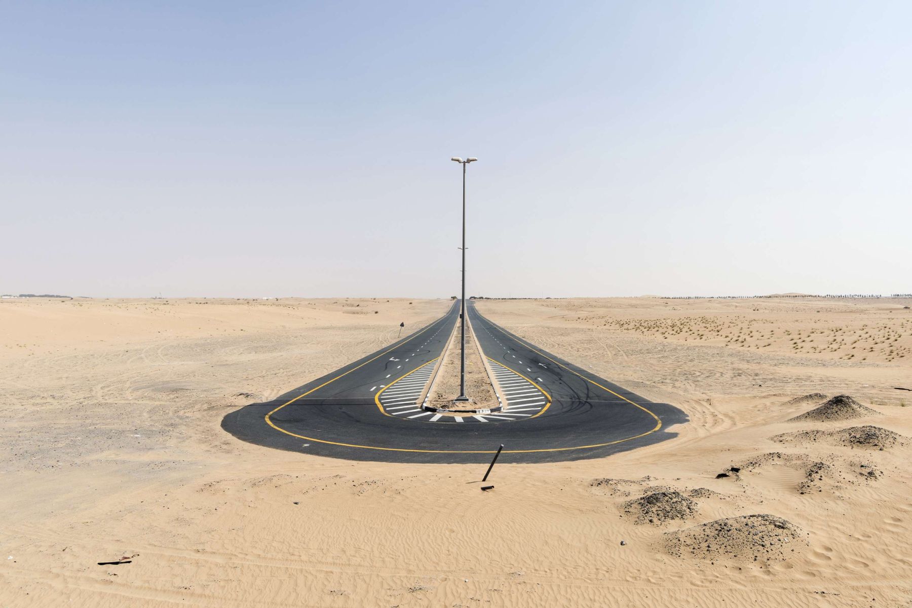 Garden of Delight by Nick Hannes — A utility pole anchors the vanishing point of an arrow-straight asphalt road bisecting flat desert terrain.