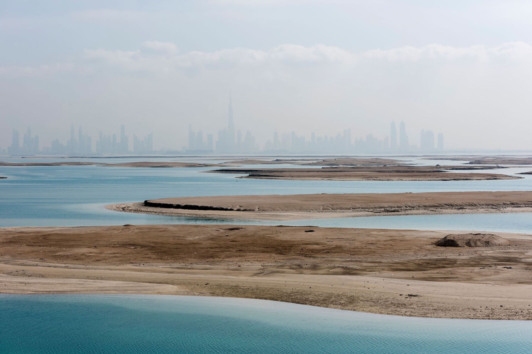 Garden of Delight by Nick Hannes — A vast tidal landscape frames Dubai's skyline across the Persian Gulf, rendered hazy in atmospheric distance.