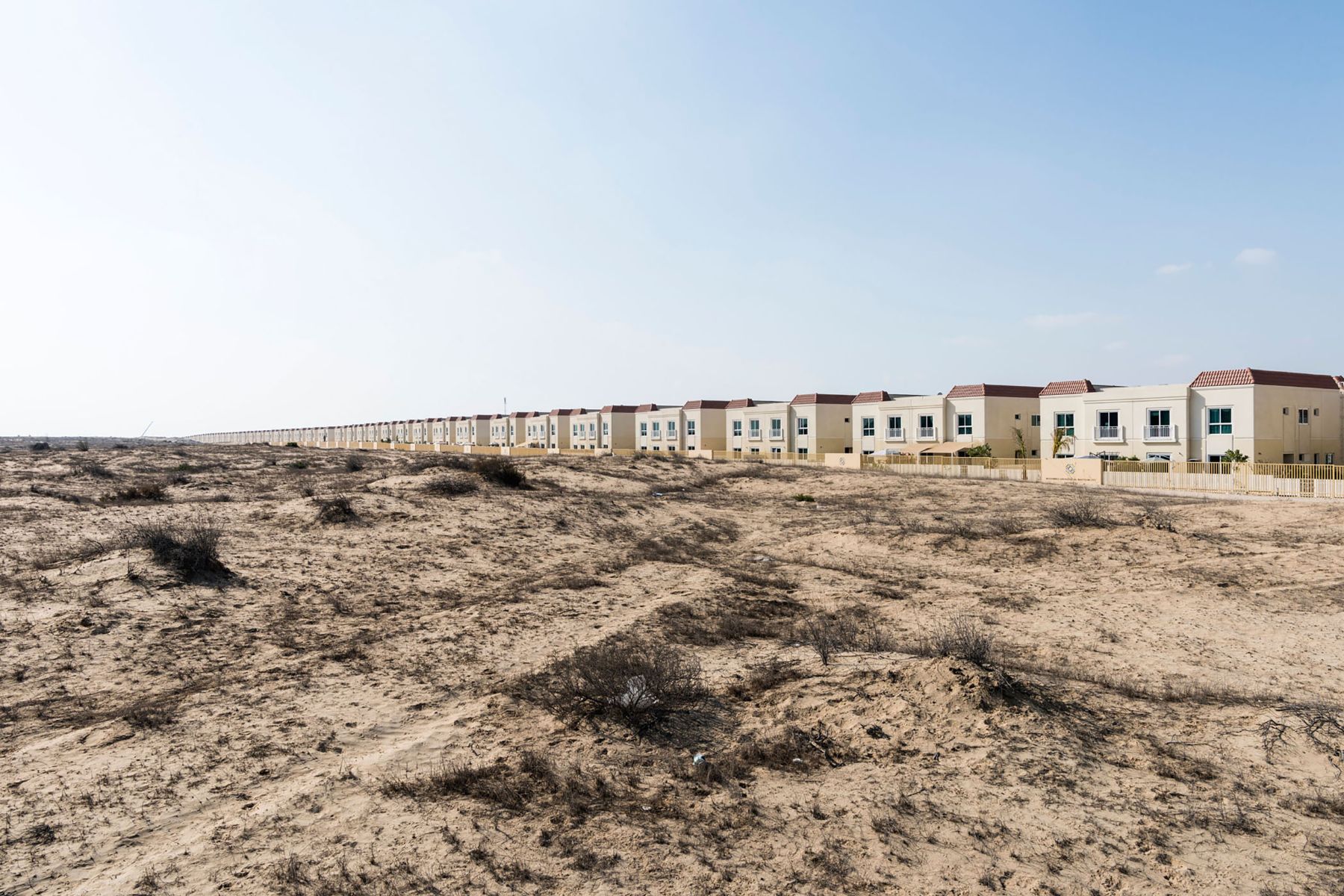 Garden of Delight by Nick Hannes — A linear row of identical cream and beige rendered townhouses extends across the desert horizon in geometric precision.