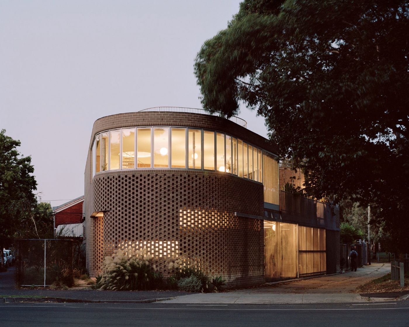 Rose House by Baracco+Wright Architects — Rose House presents as a cylindrical brick tower anchoring a triangular Melbourne site, its solid lower mass perforated by a geometric pattern of small...