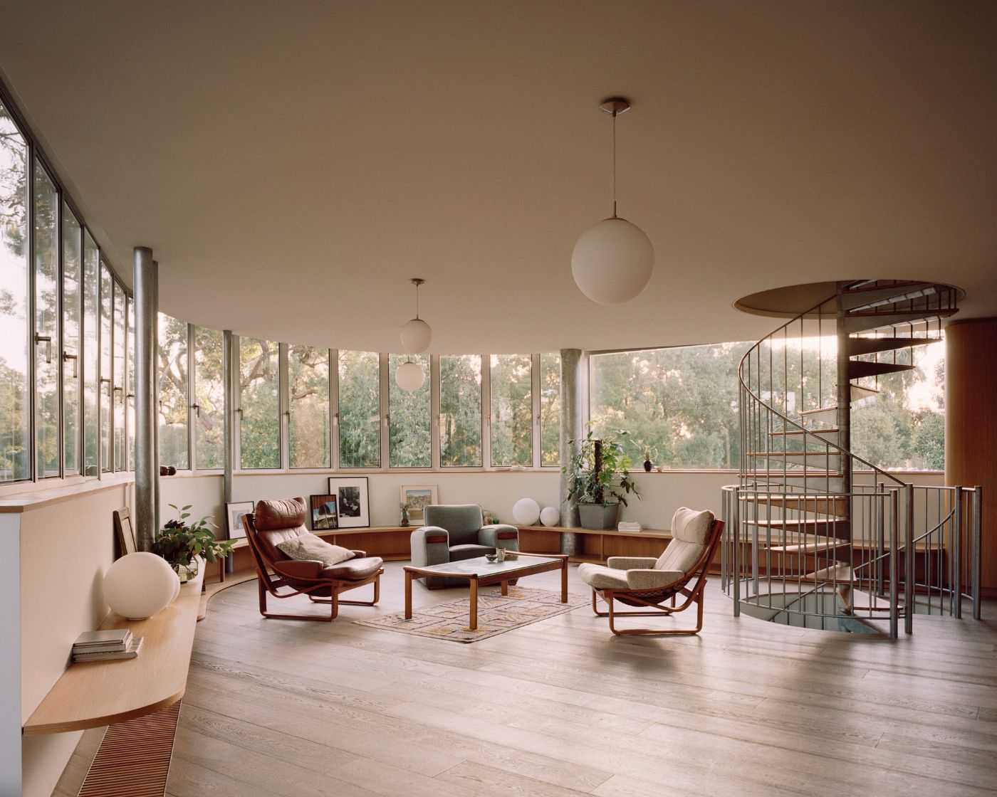 Rose House by Baracco+Wright Architects — A mid-century modern interior demonstrates open-plan living across a curved glazed facade overlooking eucalyptus forest.