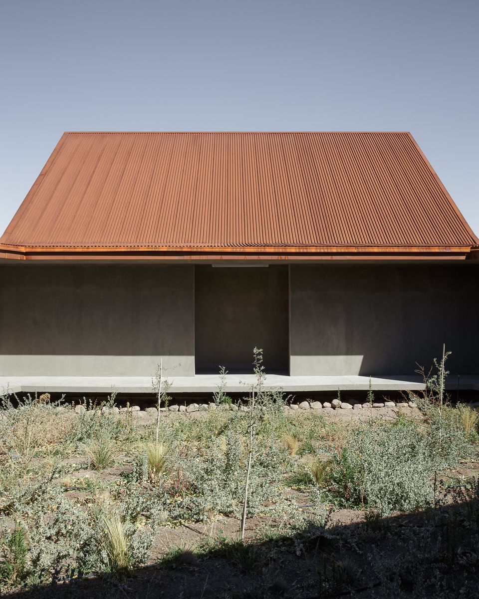 Center of Interpretation of the Desert by Emilio Marín and Juan Carlos López — A corrugated corten steel structure dominates the composition, its rust-orange roof pitched at an acute angle that echoes the distant mountain profile.