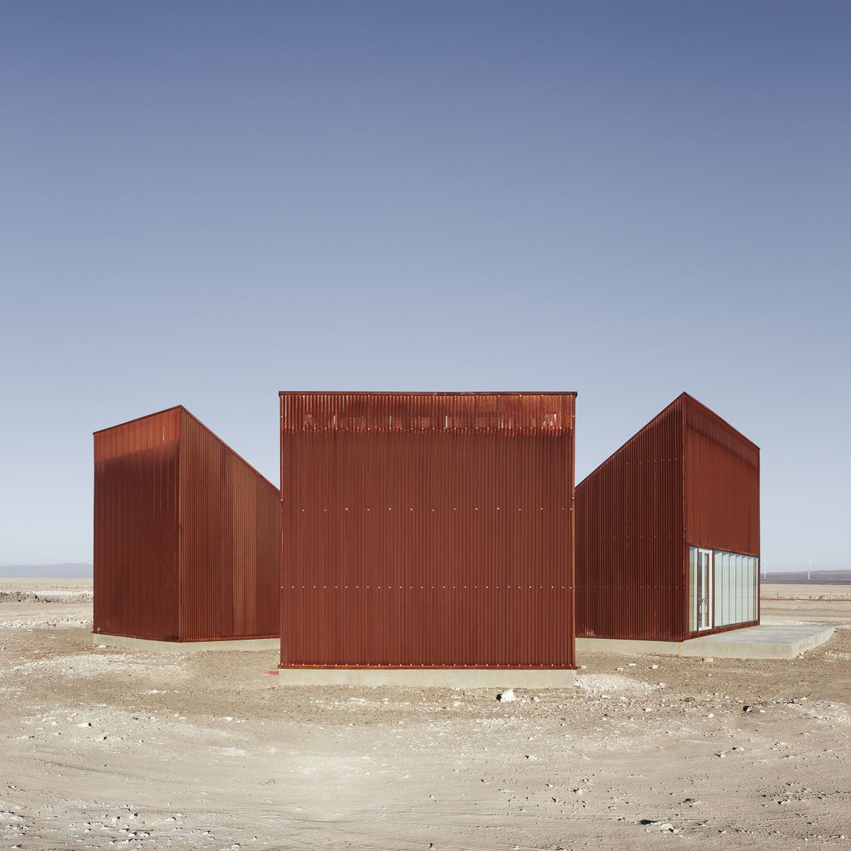 Center of Interpretation of the Desert by Emilio Marín and Juan Carlos López — Three trapezoidal volumes clad in corrugated corten steel occupy an expansive desert plain under clear blue sky.