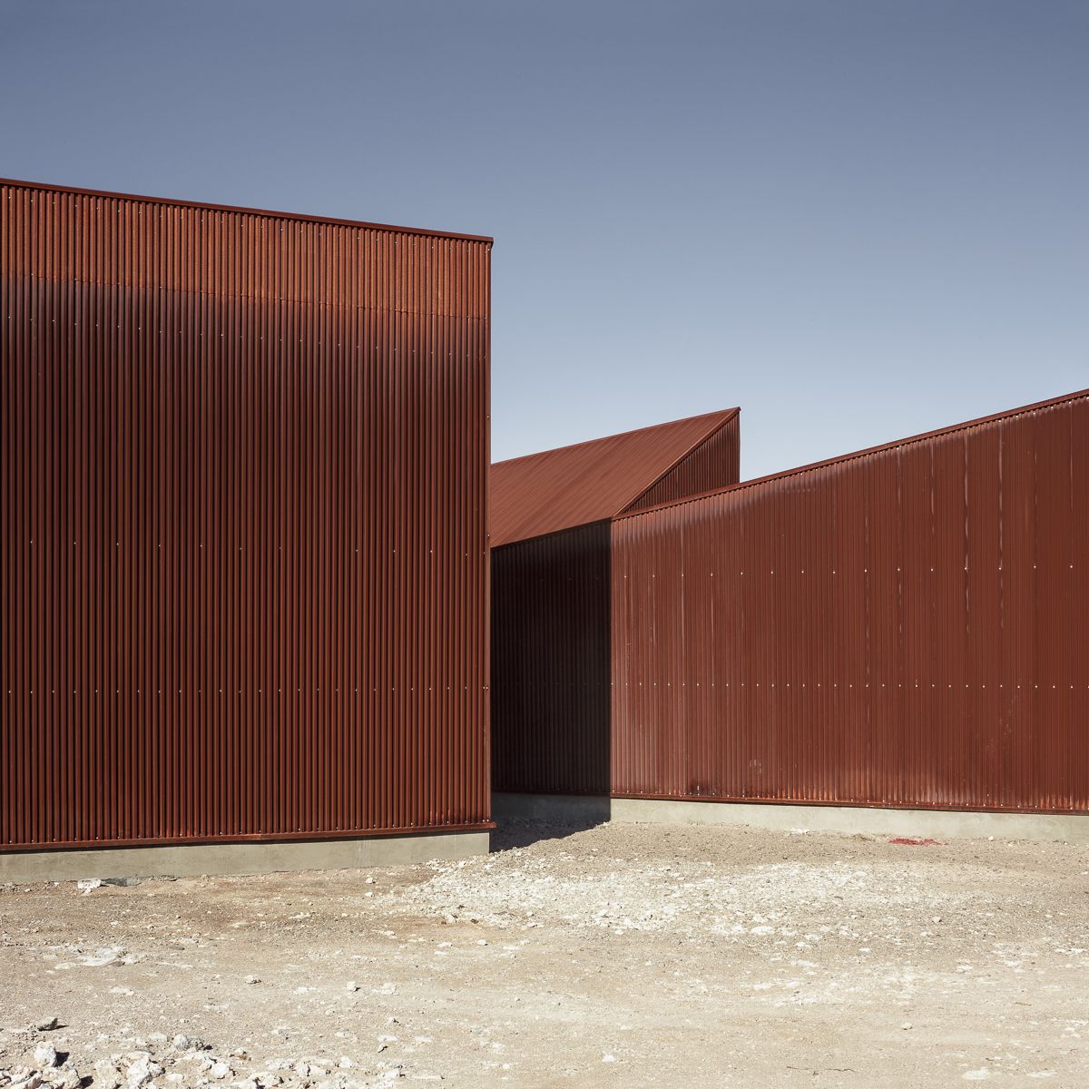 Center of Interpretation of the Desert by Emilio Marín and Juan Carlos López — Three corrugated corten steel volumes occupy a gravelly desert plain under clear sky.