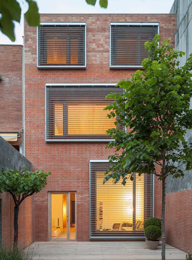 House 1014 by H Arquitectes — The street-facing elevation of House 1014 presents a studied material dialogue between its load-bearing red brick envelope and the large timber-clad sliding...