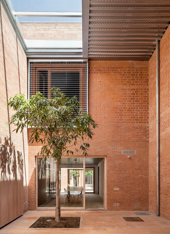 House 1014 by H Arquitectes — A narrow courtyard entry framed by unglazed red brick walls with horizontal coursing.