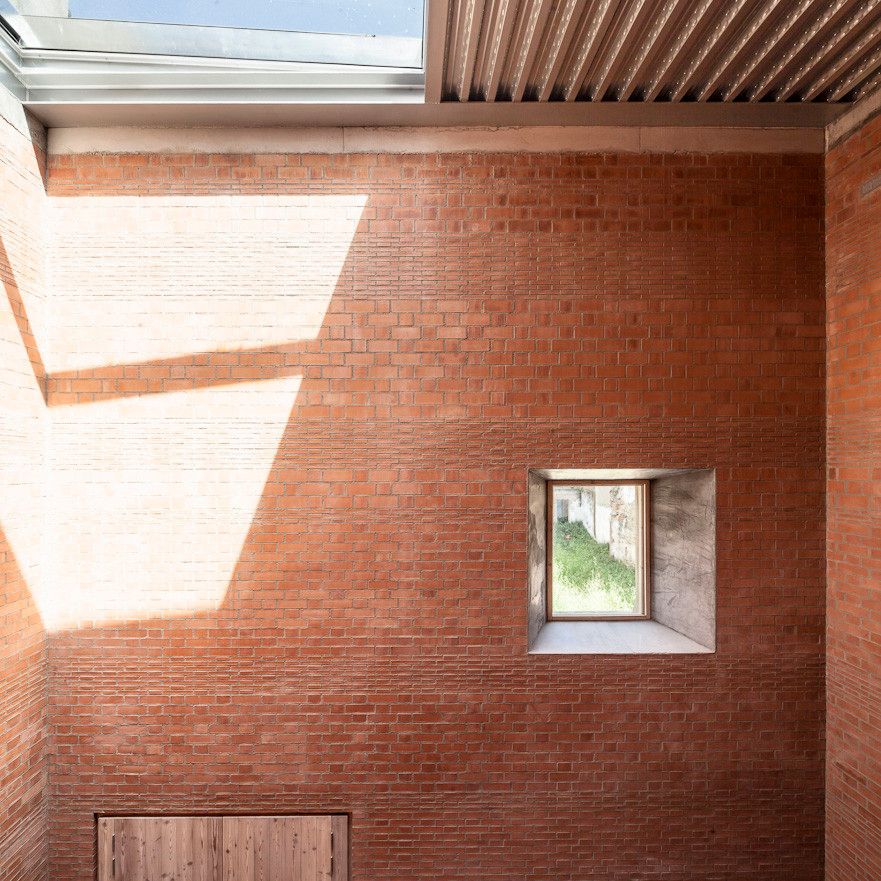 House 1014 by H Arquitectes — A narrow brick courtyard captured from interior threshold, framed by unglazed red brick walls in horizontal coursing that span the full width of the...