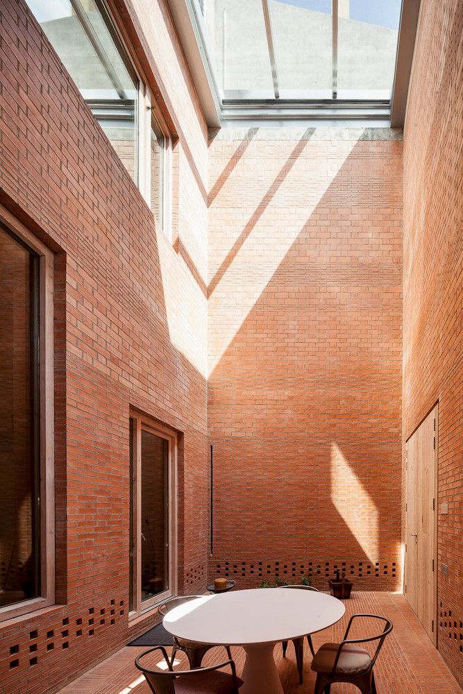 House 1014 by H Arquitectes — A narrow brick courtyard enclosed by unglazed red brick walls with horizontal coursing, accessed through a timber-framed opening.