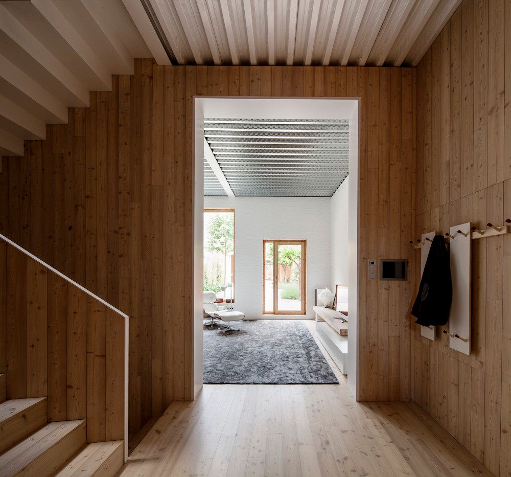House 1014 by H Arquitectes — A narrow timber-clad corridor with pine flooring connects the street-level entrance to the main living spaces.