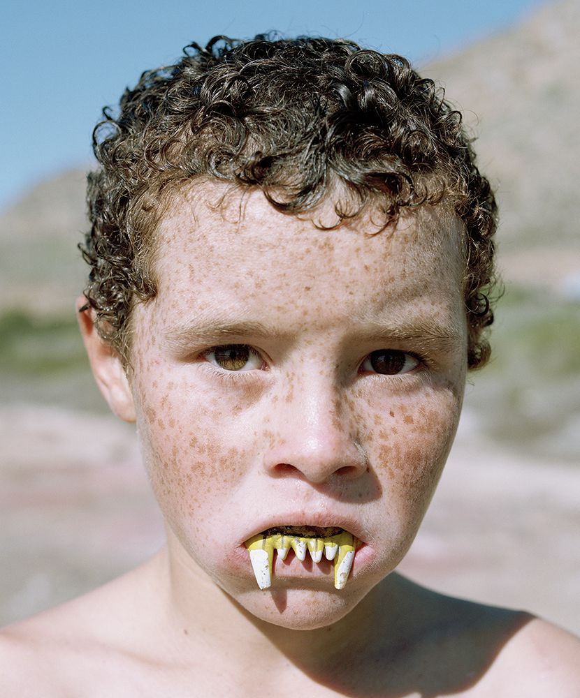 Selected works by Kent Andreasen — A close-up portrait of a figure with freckled pale skin and short curly dark hair, direct gaze confronting the camera.