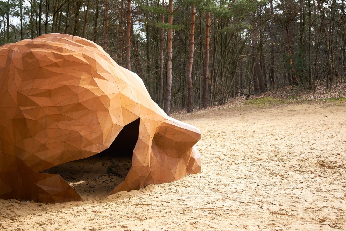 A Giant Sculpture by Gijs Van Vaerenbergh — A monumental steel sculpture with oxidized rust-orange patina occupies a sunken sandy clearing in a coniferous forest near Kasterlee, Belgium.
