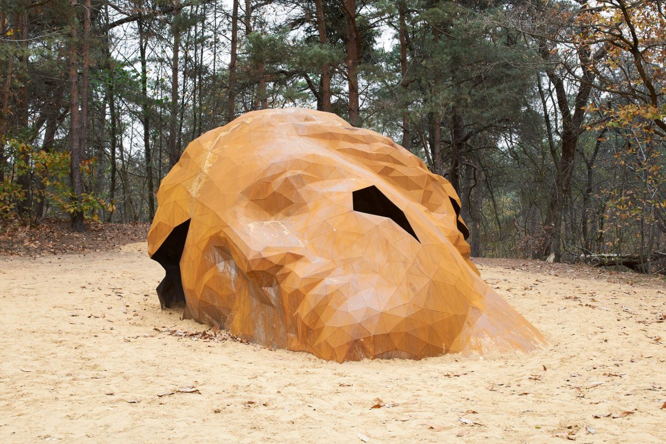 A Giant Sculpture by Gijs Van Vaerenbergh — A monumental wooden sculpture carved from a single tree trunk dominates a sandy clearing in the Hoge Mouw forest.