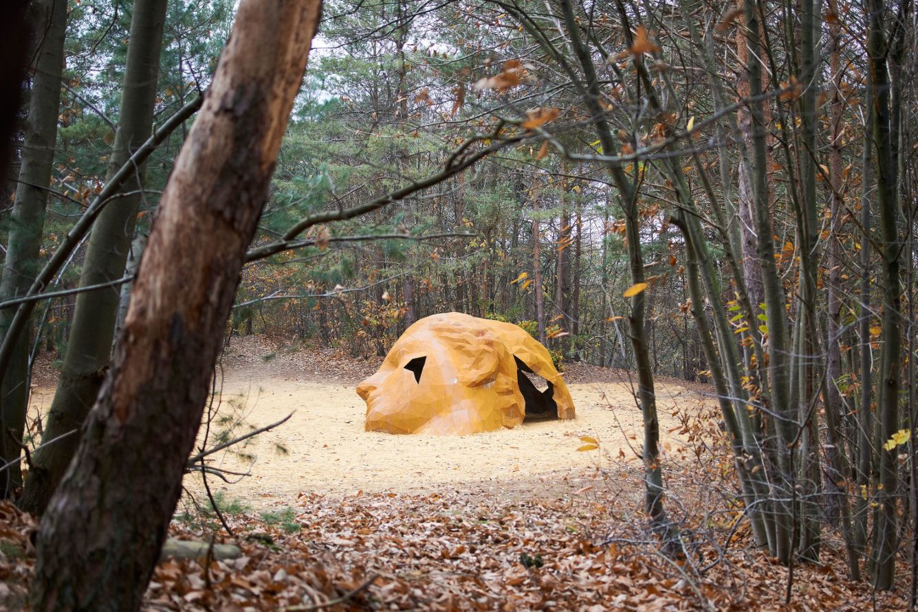 A Giant Sculpture by Gijs Van Vaerenbergh — A monumental corten steel sculpture occupies a sunken sandy clearing within a coniferous forest.