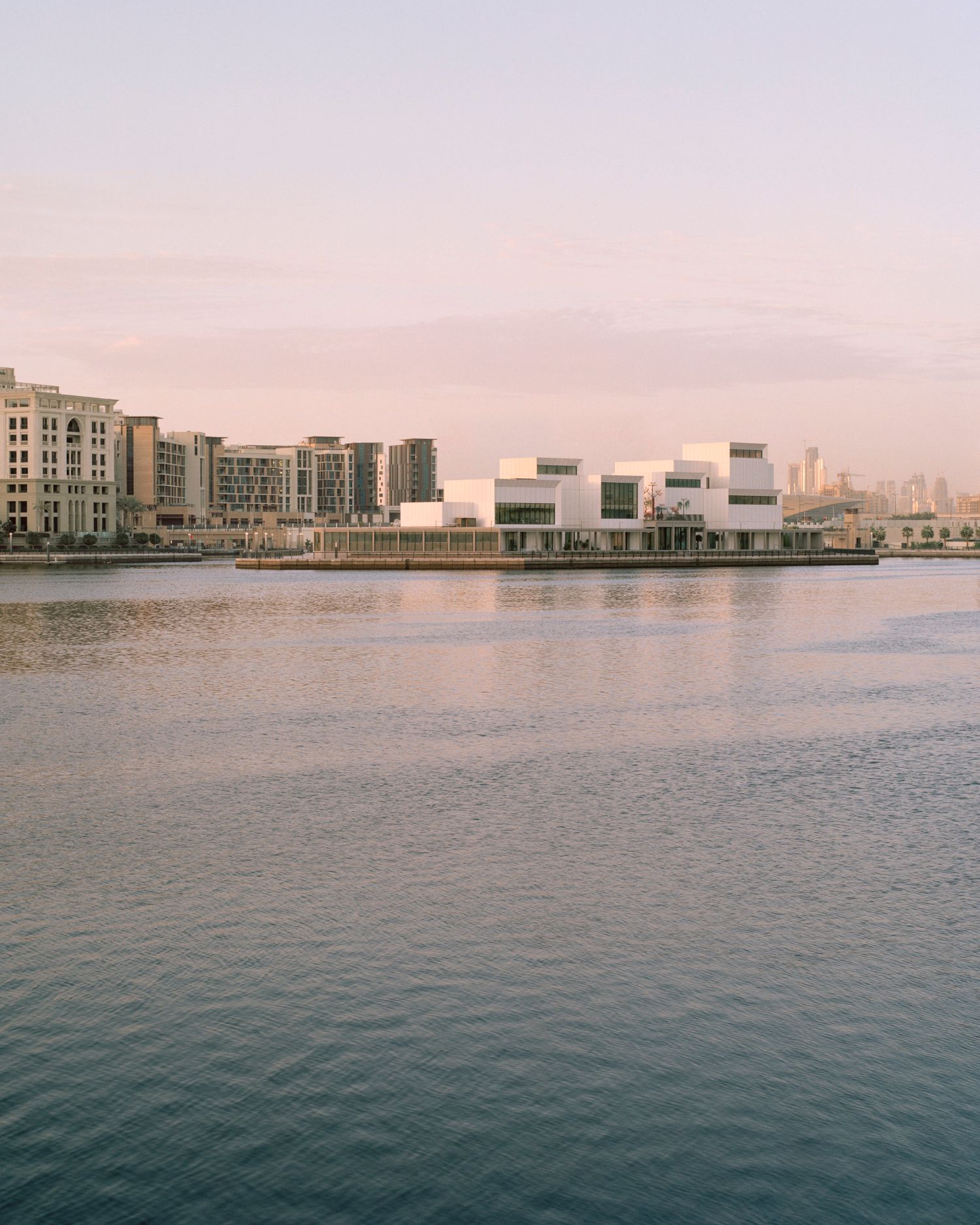 Jameel Arts Centre Dubai by Serie Architects — The Jameel Arts Centre's waterfront facade is captured during golden-hour, its corrugated white aluminum cladding with vertical ribbing catching warm light...