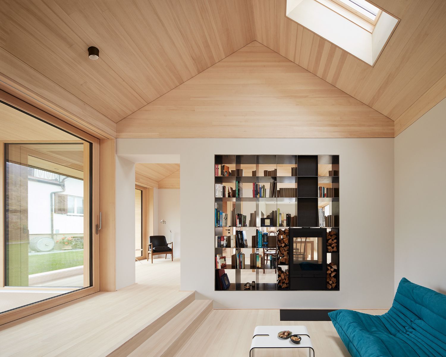 House ZF by Bernd Riegger — A pitched-timber ceiling with integrated skylights frames the living space in House ZF, creating a geometric interior volume.