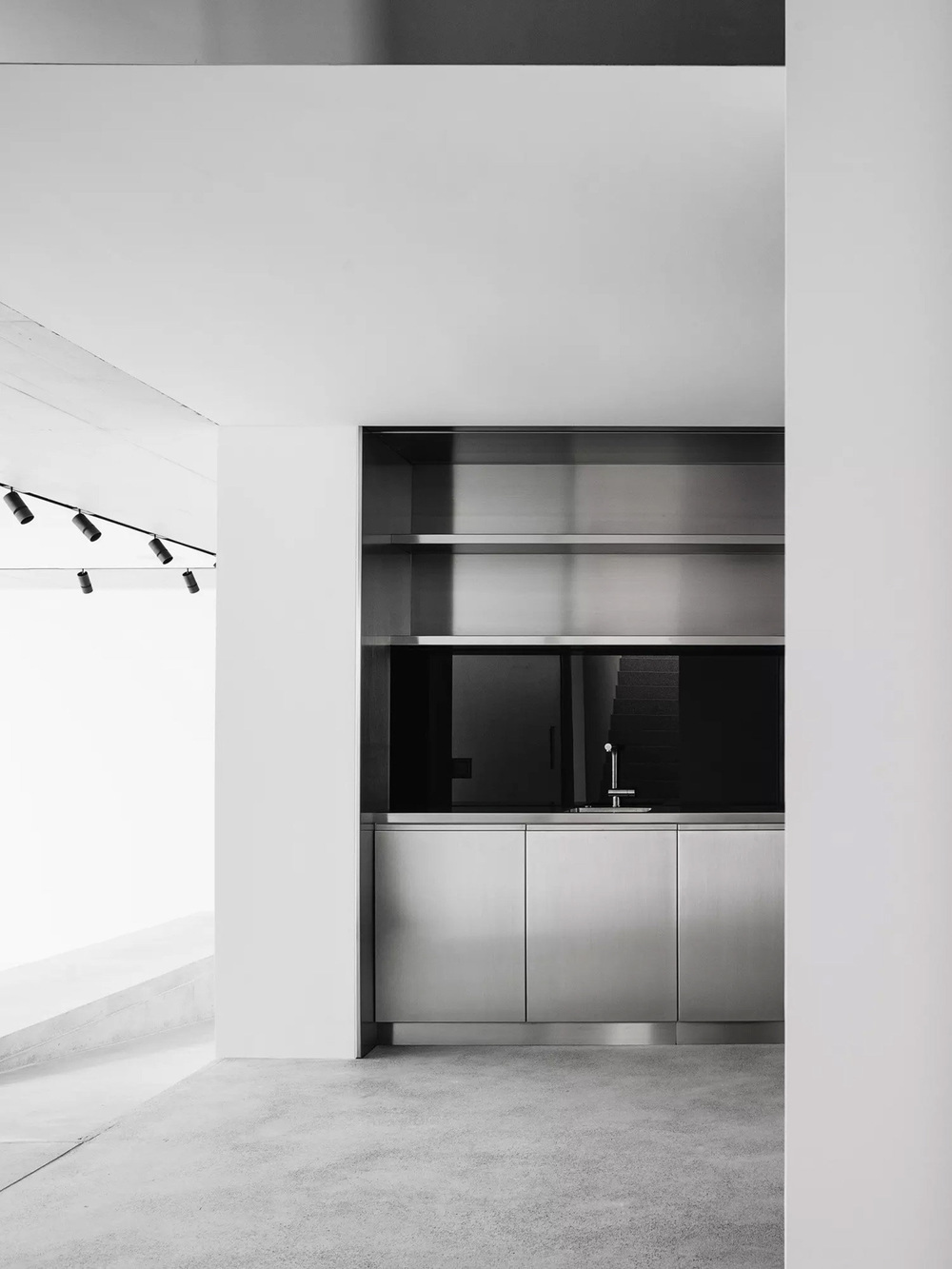 House for an Art Collector by Think Architecture — A kitchen alcove recessed into white walls, fronted by a horizontal composition of stainless steel cabinetry with three flush-mounted drawers.