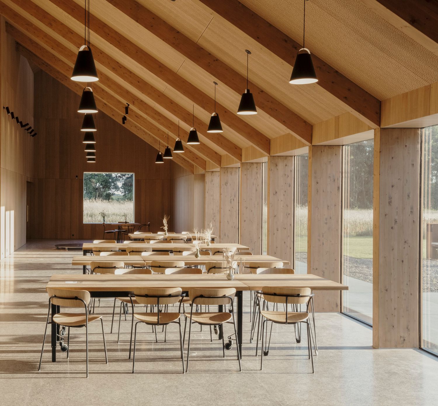House of Grain by Reiulf Ramstad Arkitekter — Interior view of the dining and gathering space within House of Grain, revealing the post-and-beam timber structure supporting steeply pitched roof planes...
