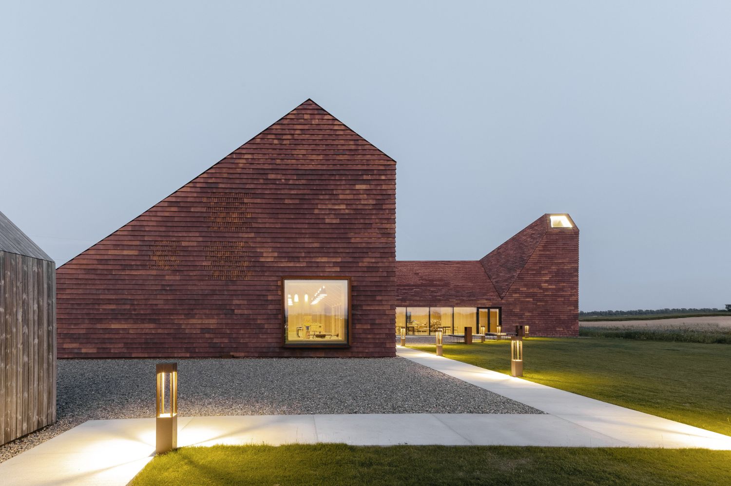 House of Grain by Reiulf Ramstad Arkitekter — The grain house's twin pyramidal brick towers dominate the flat Jutland landscape at dusk, their steeply pitched roofs creating sharp silhouettes against a...