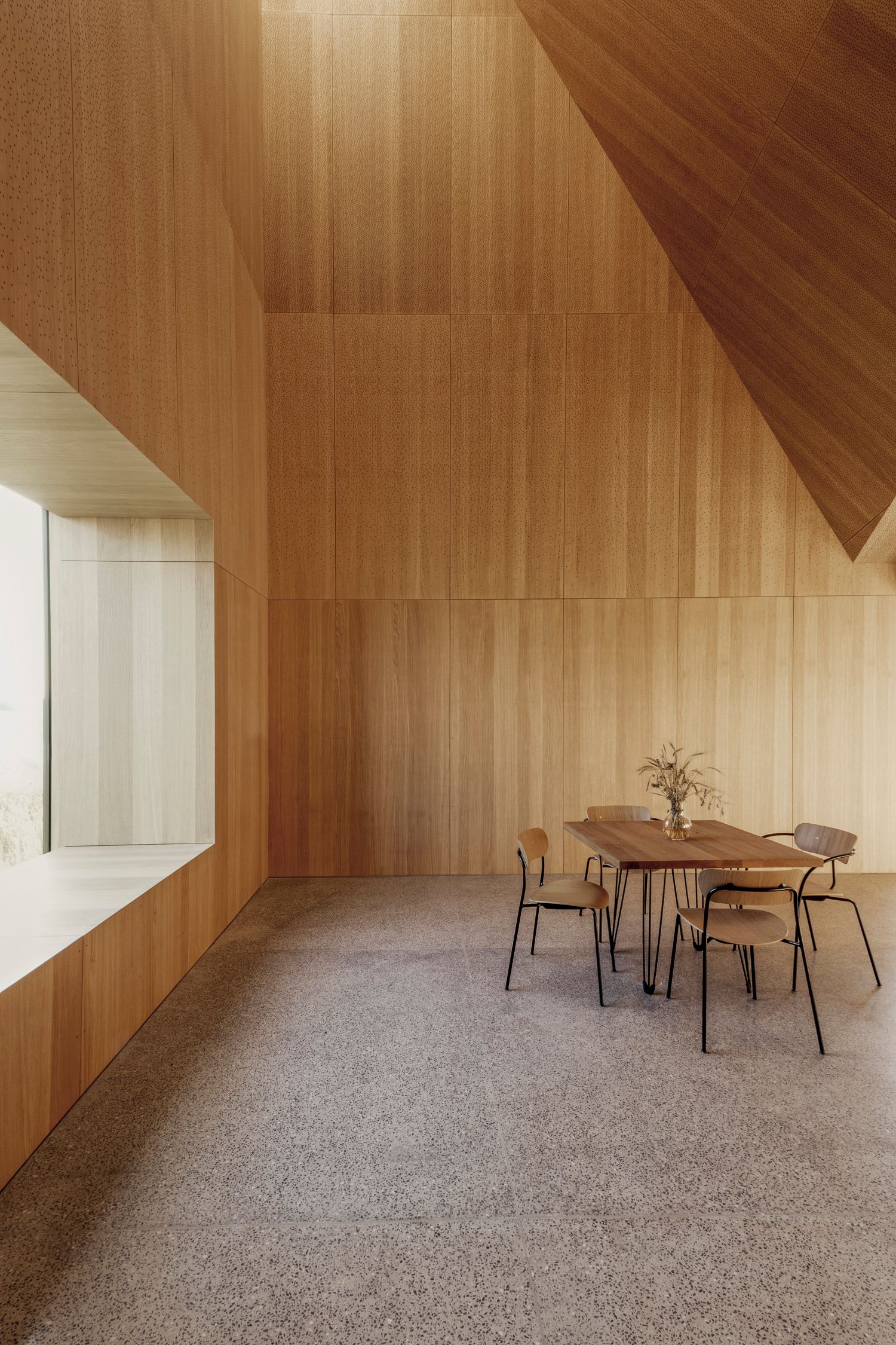 House of Grain by Reiulf Ramstad Arkitekter — Interior view of the grain house dining space, defined by continuous vertical wood paneling in warm honey and amber tones covering walls and ceiling.