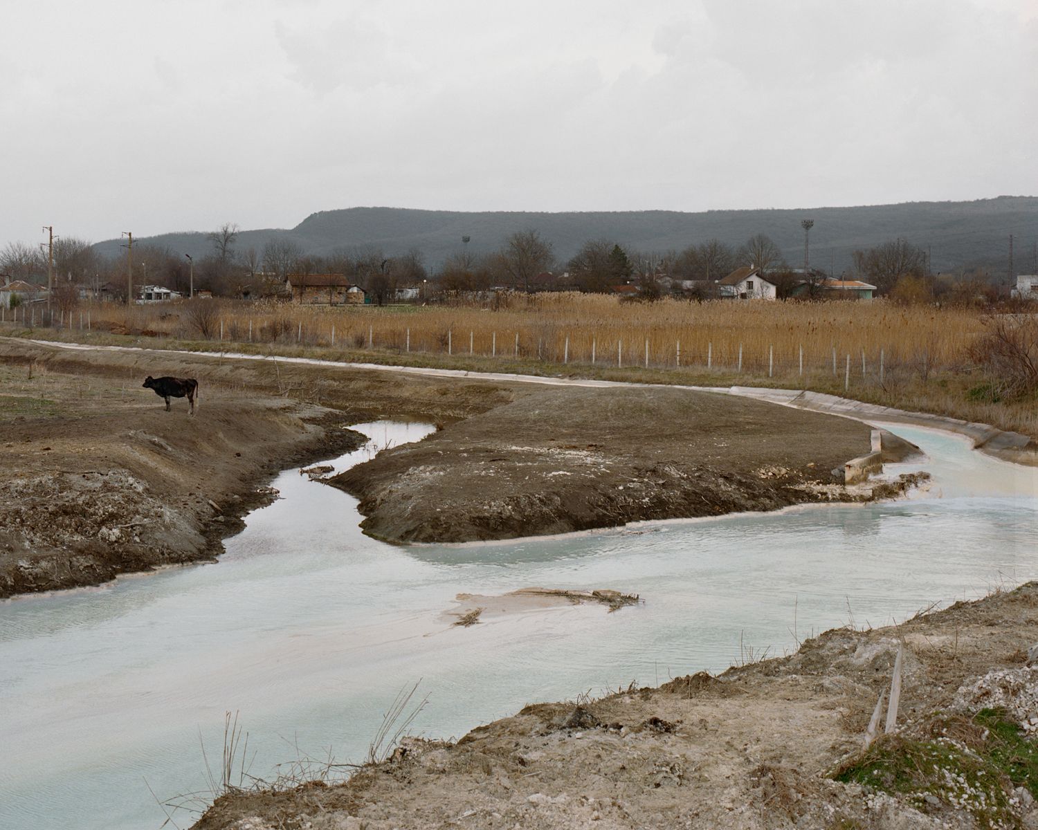Along the Swift Current of Time by Teodora Georgieva — A rendered landscape of industrial aftermath in Devnya, Bulgaria, captures turquoise-tinted water pooling across barren sediment with visible mineral...