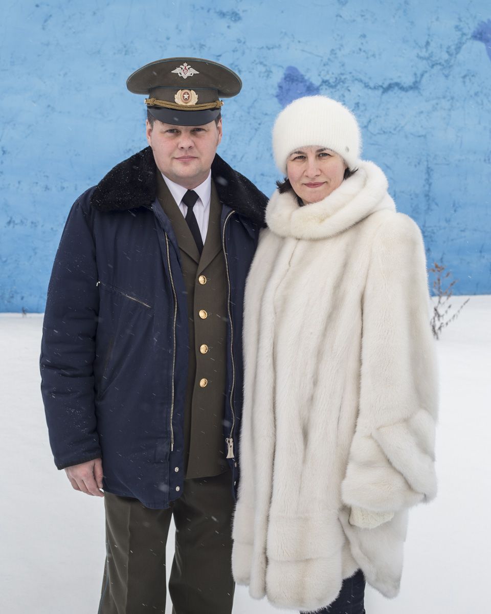 Удачный / Lucky by Hanne Van Assche — A portrait of two figures standing against a vivid blue wall with snow accumulation at ground level.