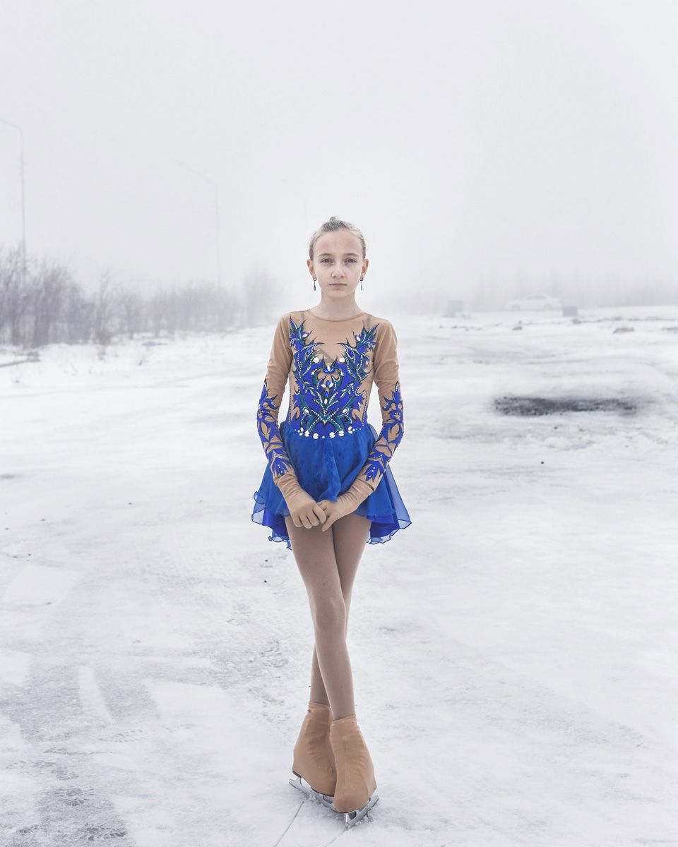 Удачный / Lucky by Hanne Van Assche — A young figure in a cobalt-blue competition figure-skating dress stands centered on a frozen river surface in Udachny, Yakutia.