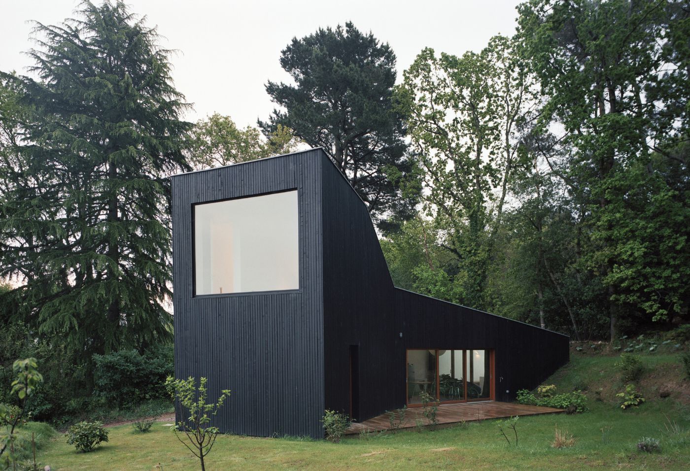 Holiday House in Sarzeau by RAUM — A dark-clad structure dominates the forest clearing, its charcoal corrugated metal facade rising as a monolithic tower.