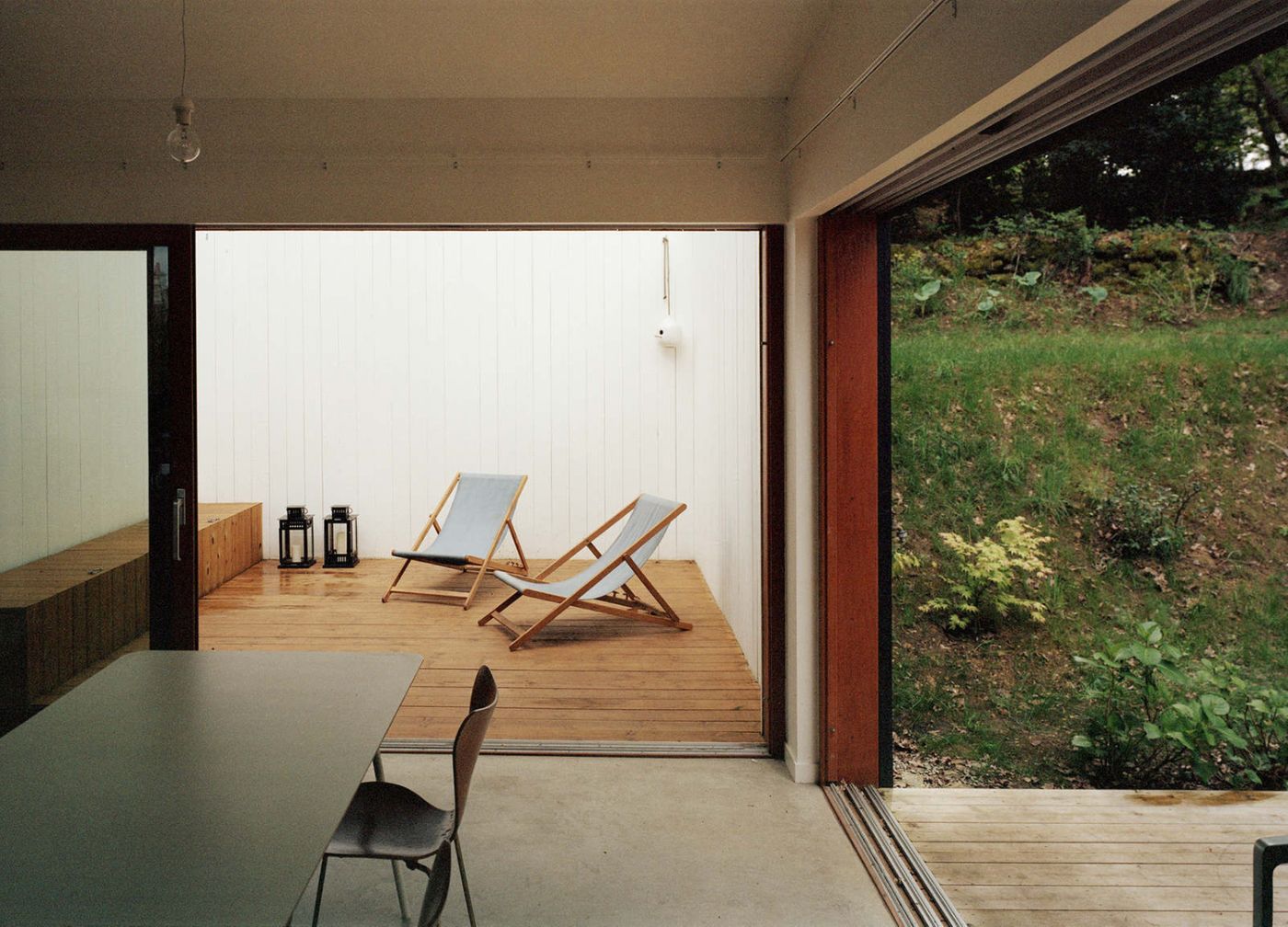 Holiday House in Sarzeau by RAUM — The ground floor living area frames a wooden deck and garden-facing courtyard through a large horizontal glazing.