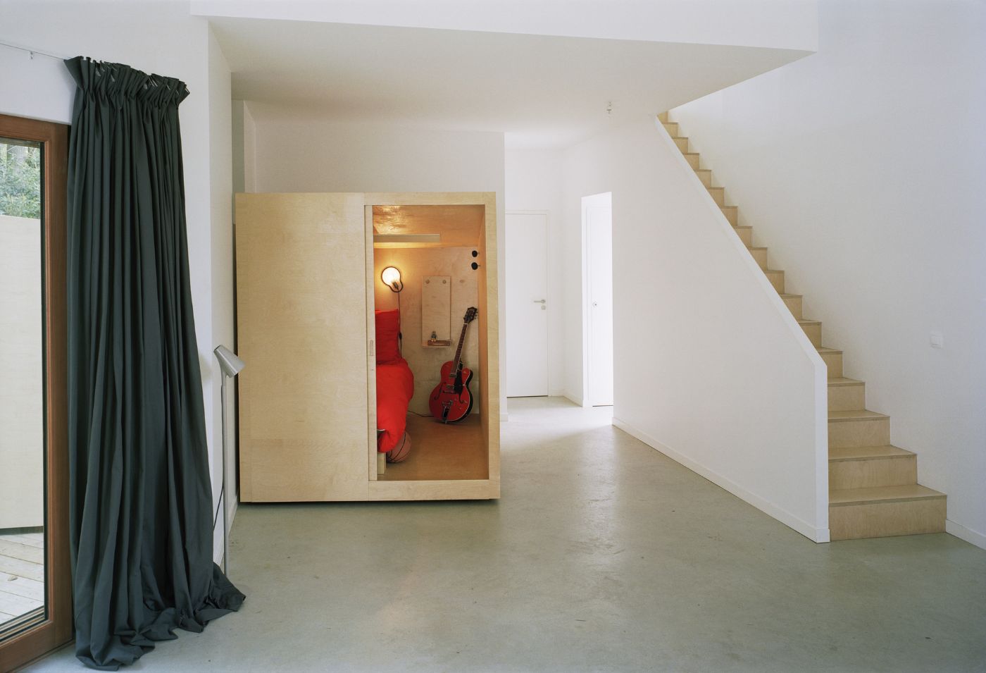 Holiday House in Sarzeau by RAUM — A double-height interior volume with a monolithic white staircase anchoring the right wall.