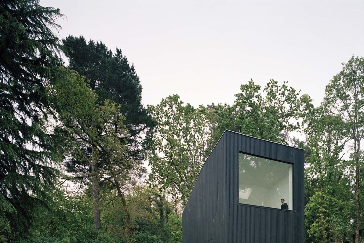 Holiday House in Sarzeau by RAUM — A tower-form structure clad in vertical corrugated metal in charcoal finish rises from a densely forested setting in Sarzeau.