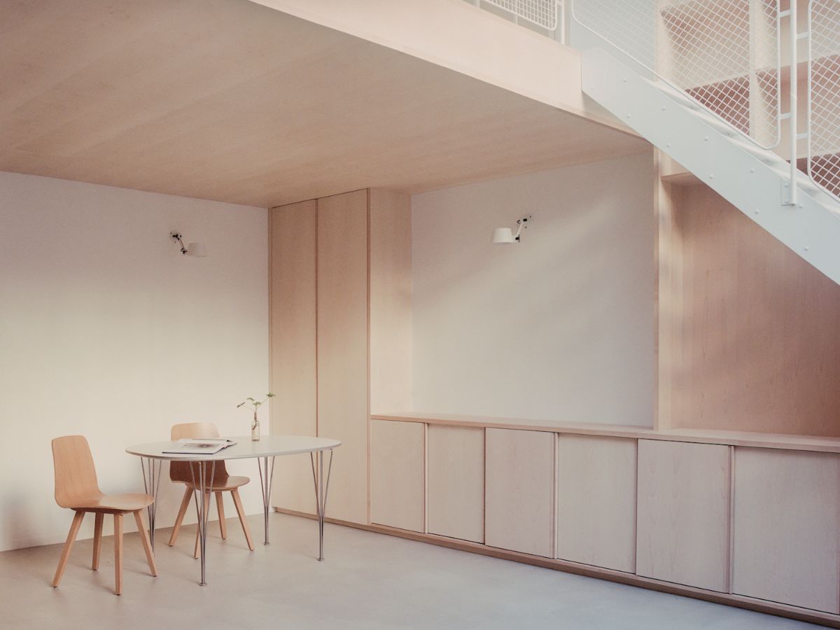 Jean Moulin Atelier – House by Atelier NEA — A compact studio workspace beneath a sloped ceiling plane features custom light oak cabinetry with flush joinery along the left wall, topped by a continuous...