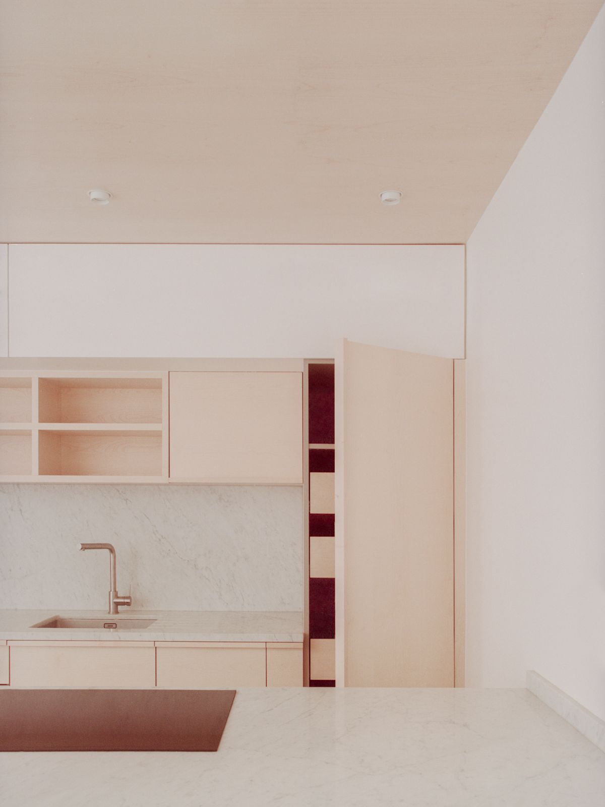 Jean Moulin Atelier – House by Atelier NEA — The kitchen workspace features custom light oak cabinetry with flush joinery aligned along the left wall, anchored by a copper-toned sink fixture.